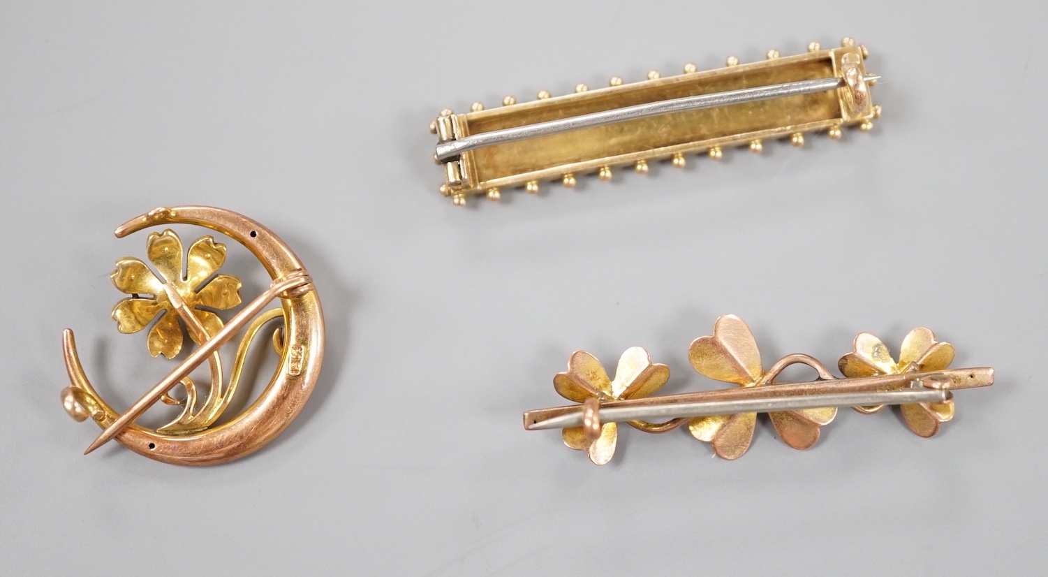 A late Victorian 15ct and seed pearl set flower and crescent brooch, 22mm, gross 3.1 grams and two later yellow metal bar brooches, gross 6 grams.